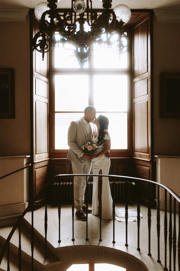 Les mariés enlacés devant une grande fenêtre sous un lustre, mariage à Bouillon