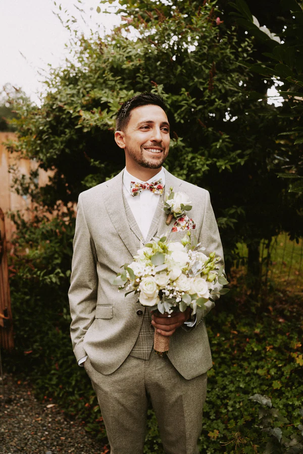 Le marié en costume gris clair avec son bouquet blanc, mariage au Primordia