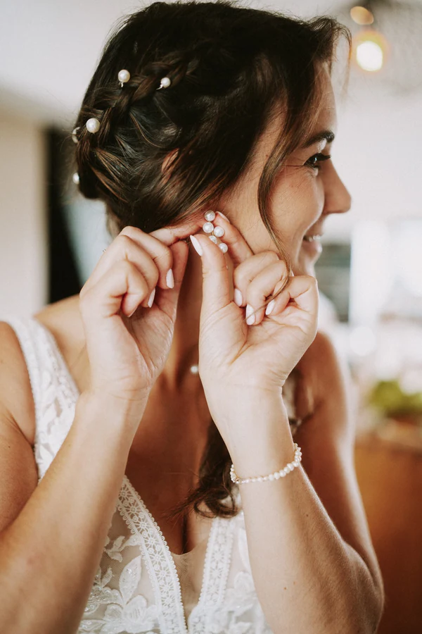 La mariée met ses boucles d'oreilles, gros plan, mariage au Primordia