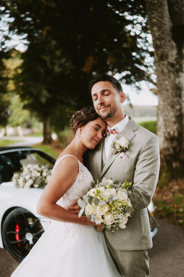 Les mariés enlacés contre le cabriolet blanc, mariage au Primordia