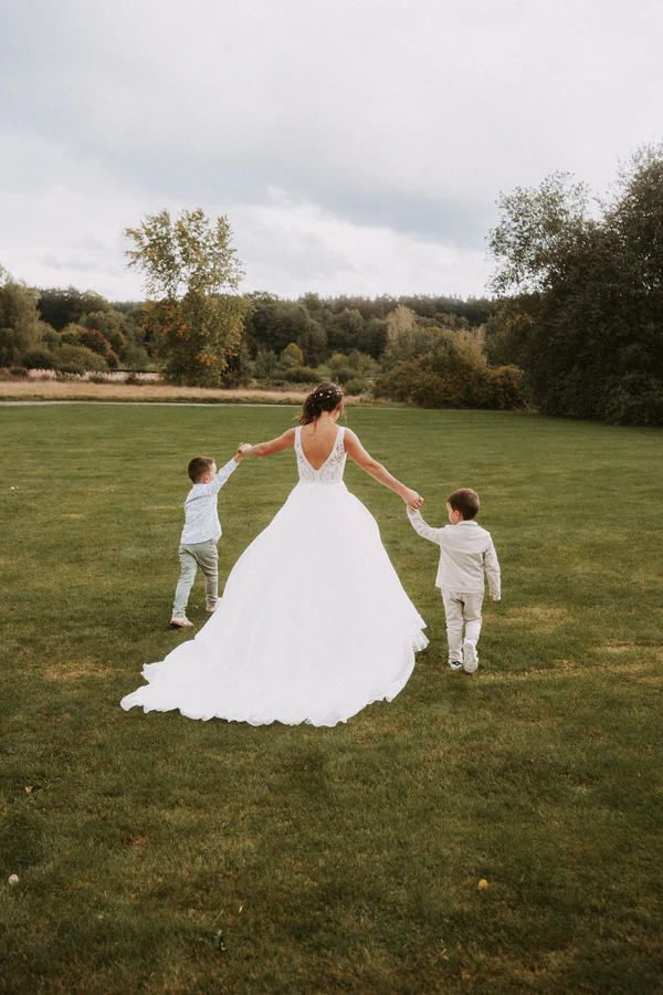 La mariée de dos marche sur la pelouse avec deux petits garçons, mariage au Primordia