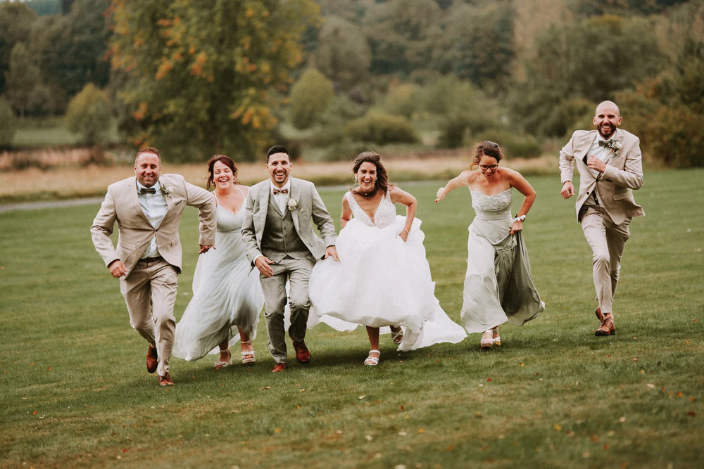 Les mariés et leurs proches courent sur la pelouse, mariage au Primordia