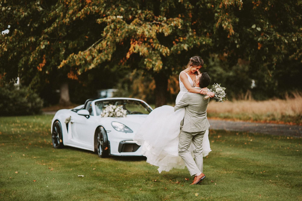 Les mariés et leur cabriolet blanc dans un décor boisé, mariage au Primordia