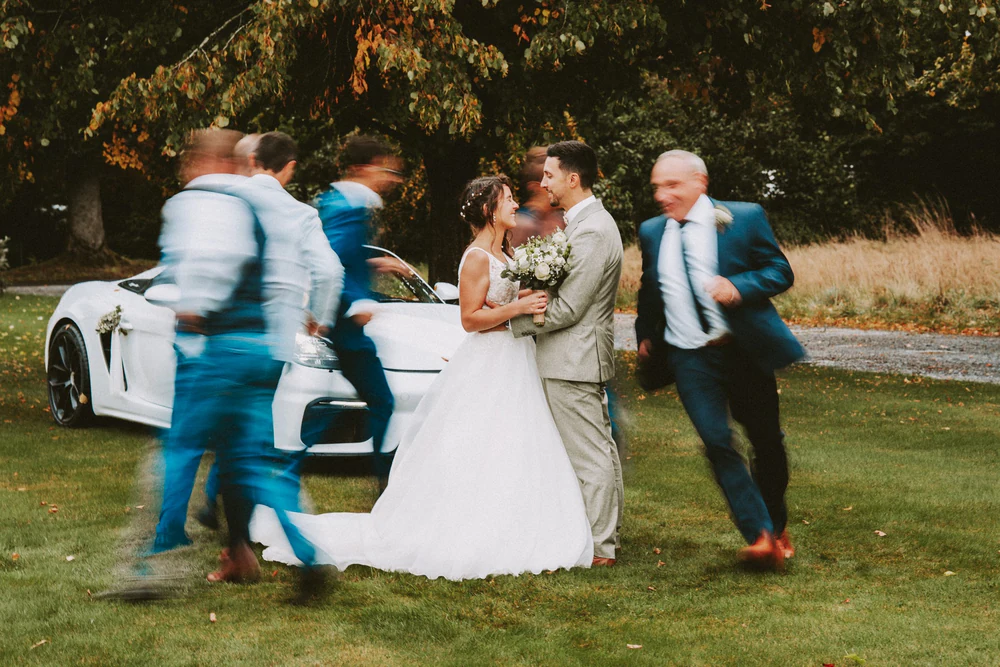 Les mariés et leurs proches rient près du cabriolet, mariage au Primordia