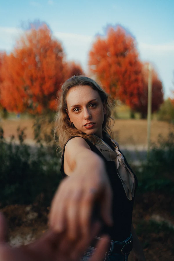 Portrait de Chloé, regard par-dessus l'épaule et main tendue vers l'objectif, arbres d'automne orangés, par Gautier Collet