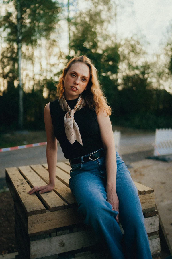 Portrait de Chloé assise sur des palettes en bois, foulard et jean, lumière douce du soir, par Gautier Collet