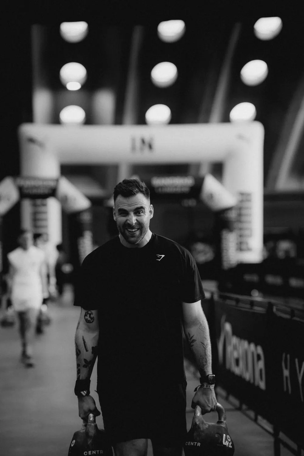 Gautier Collet souriant, un kettlebell dans chaque main, photo en noir et blanc