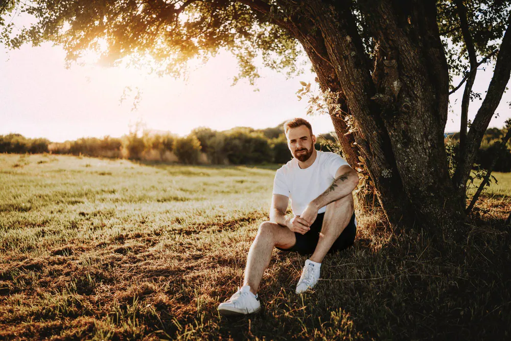 Gautier Collet, photographe de mariage, assis dans l'herbe sous un arbre au coucher du soleil