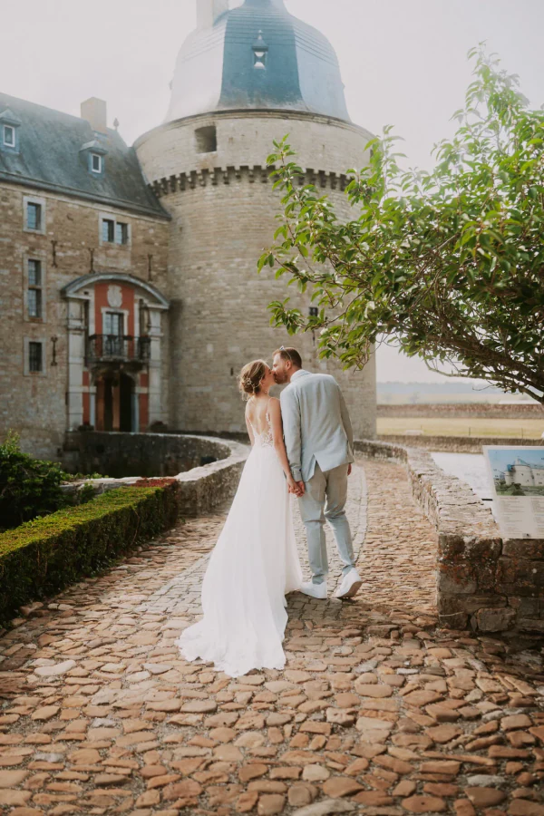 Les mariés s'embrassent sur le chemin pavé, devant la tour du château et ses haies de buis