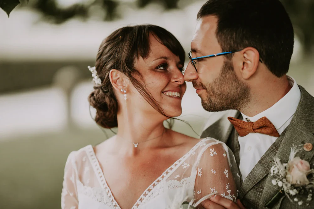 Les mariés nez contre nez et souriants, lui à lunettes et nœud papillon orange, elle en robe de dentelle