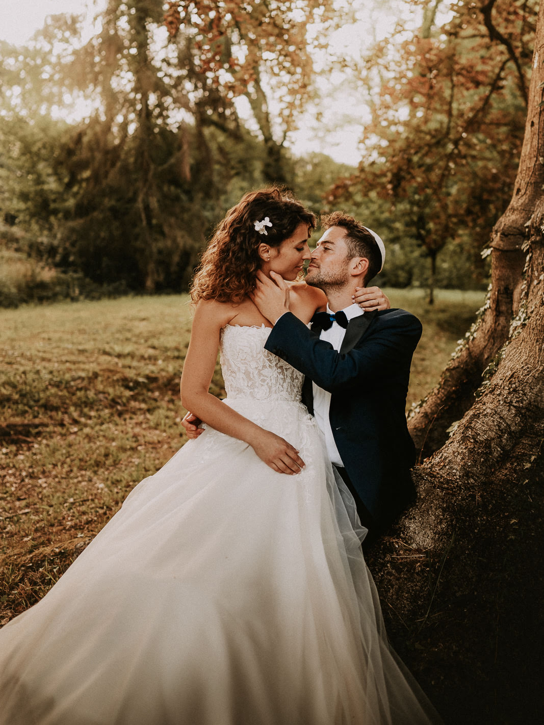 une mariée et un marié appuyés contre un arbre.